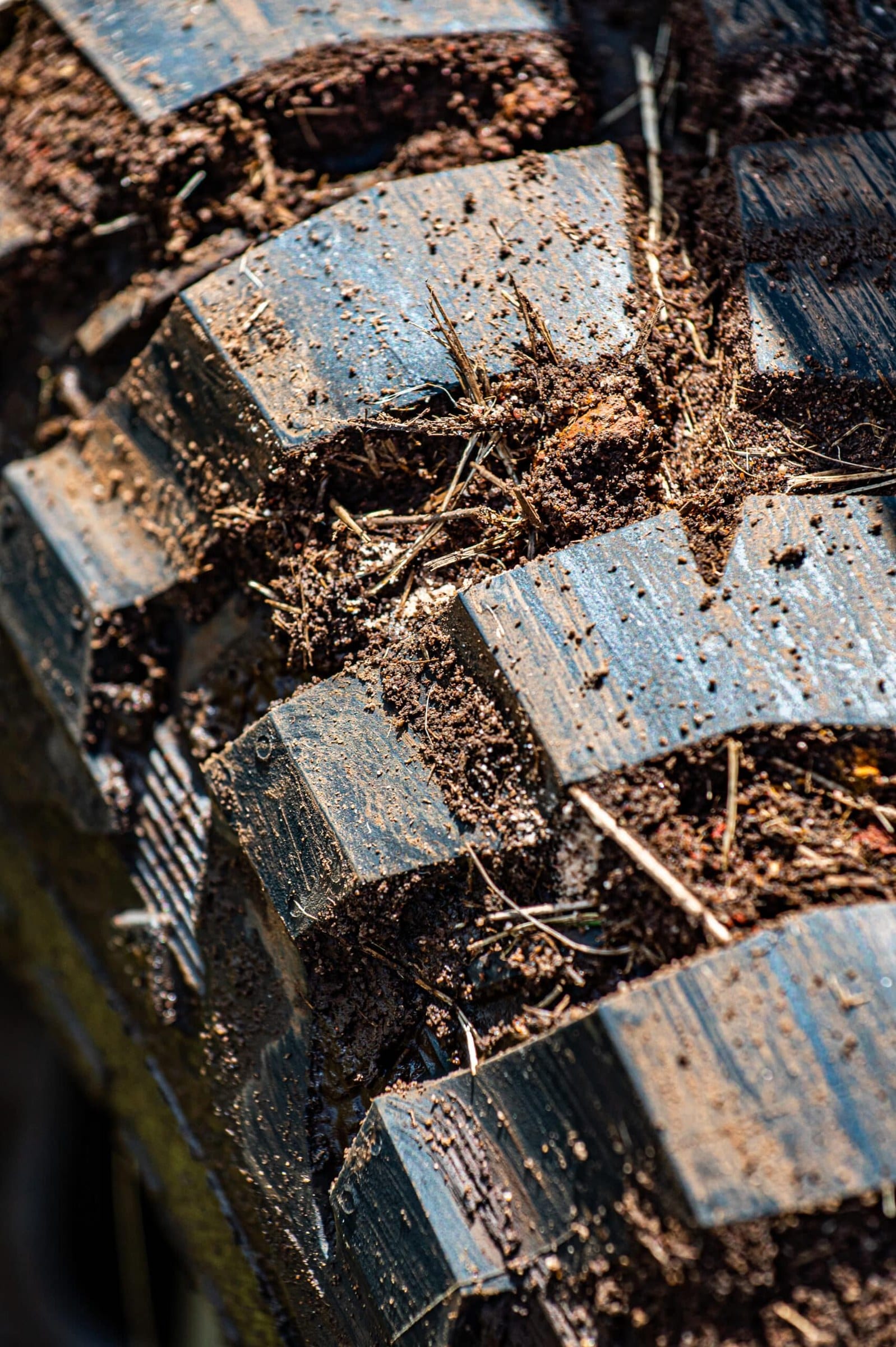 A close-up of mud-terrain tyre tread blocks packed with red mud and dry grass