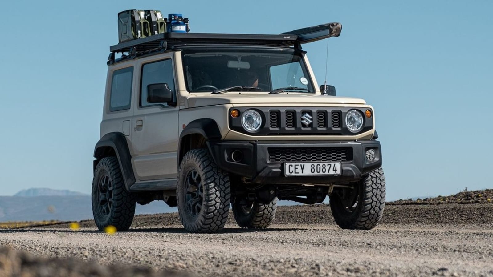A beige current Suzuki Jimny 3-door on General all-terrain tyres, parked on gravel in the Tankwa Karoo with a loaded roof rack