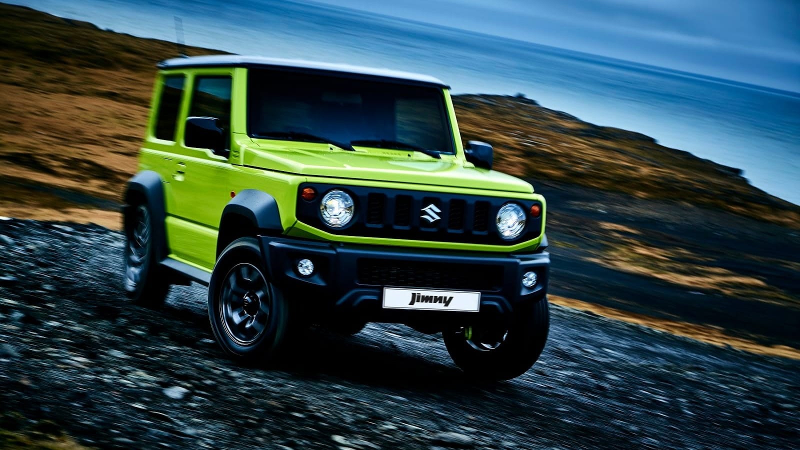 A lime green, standard Suzuki Jimny 3-door driving along a gravel road above the sea