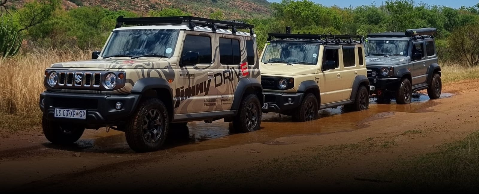 Three Suzuki Jimny 5-doors in a line on a wet dirt track, the first one wrapped in Jimny Drive graphics