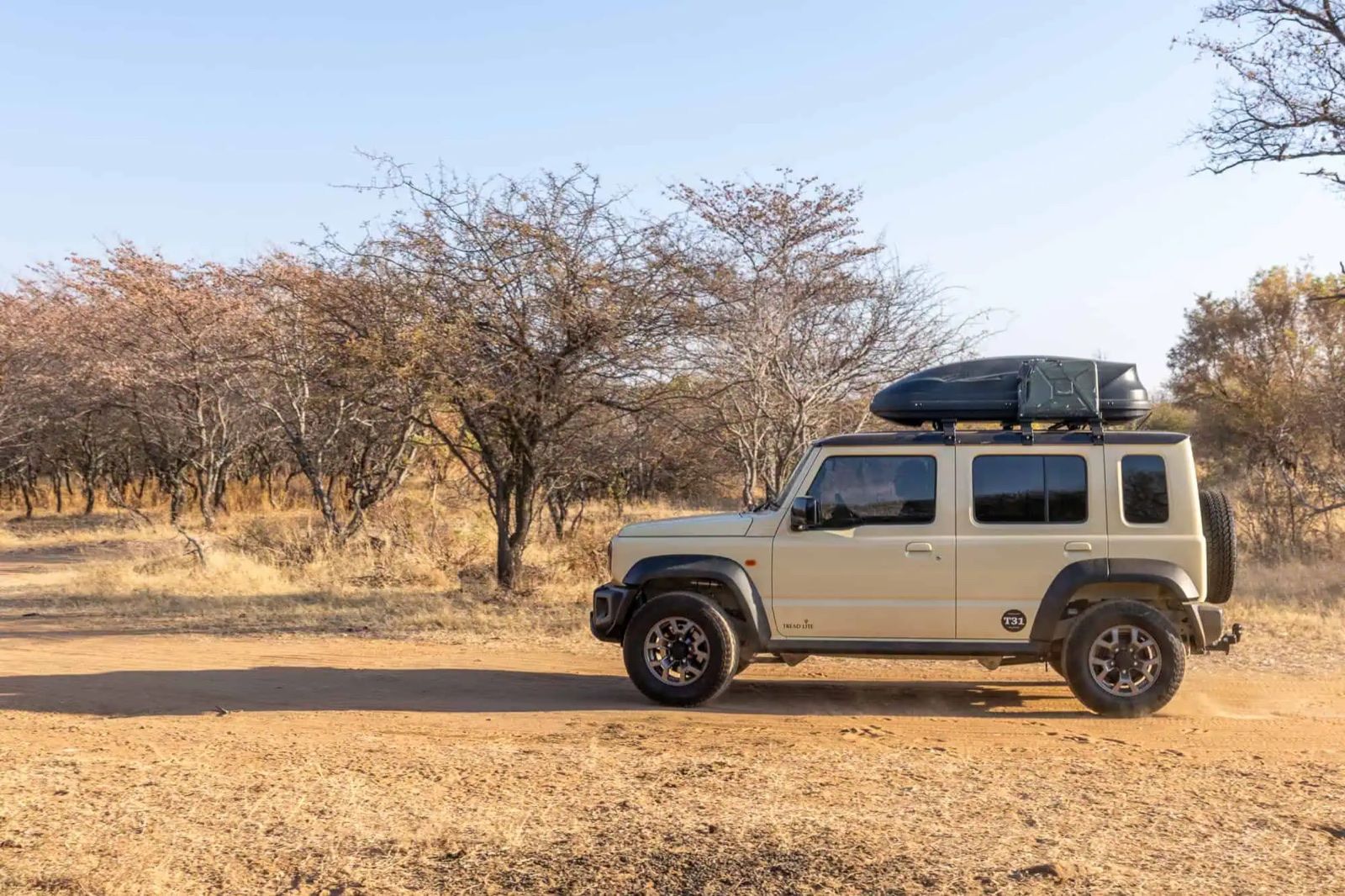 A 5-door Suzuki Jimny with a roof box parked on a bushveld track in South Africa