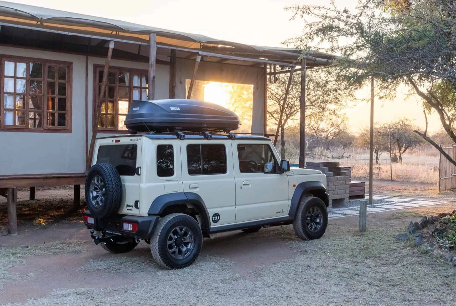 A 5-door Suzuki Jimny with a rooftop box at a bush camp at sunset in South Africa