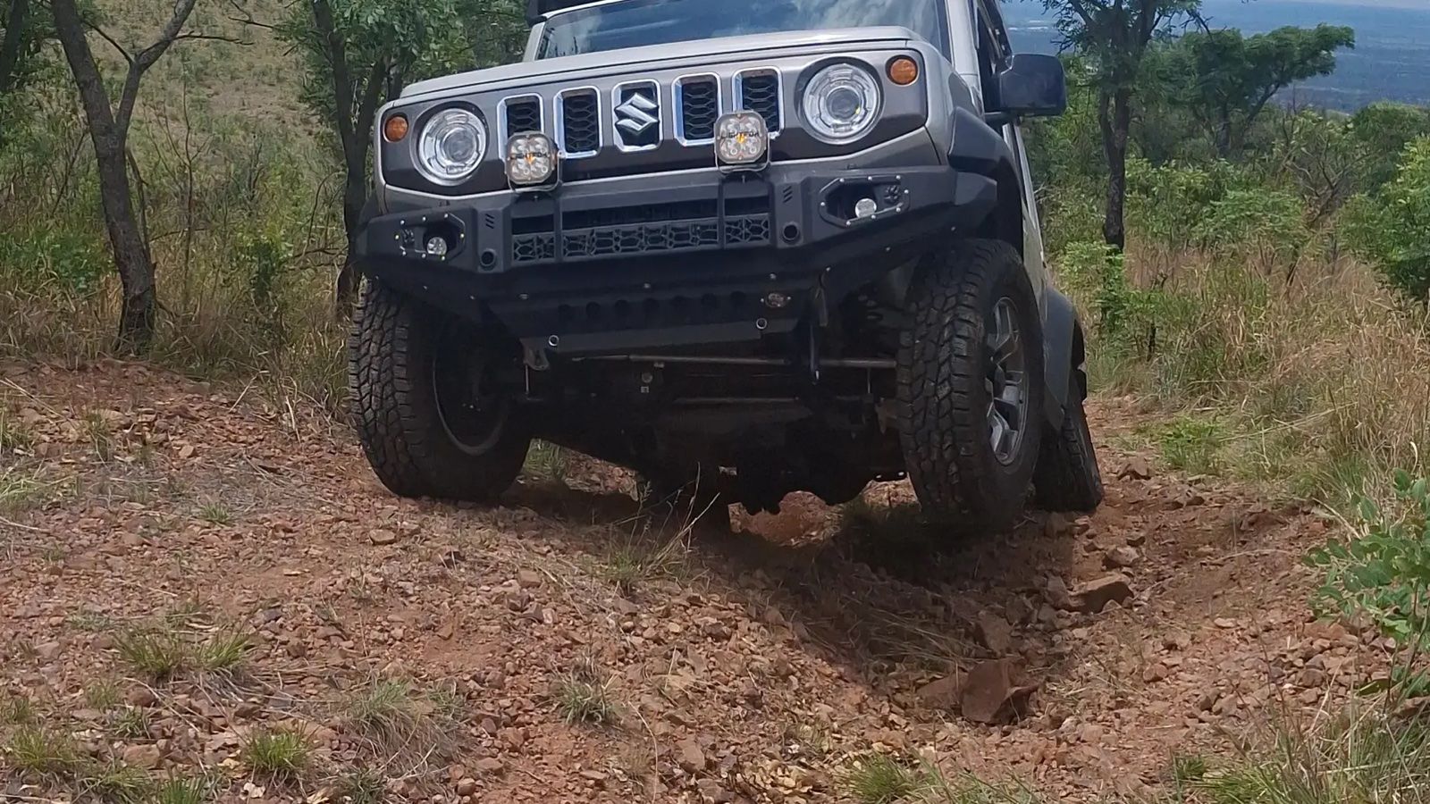 A Suzuki Jimny crawling over a rocky off-road obstacle, front wheels flexing over the rocks