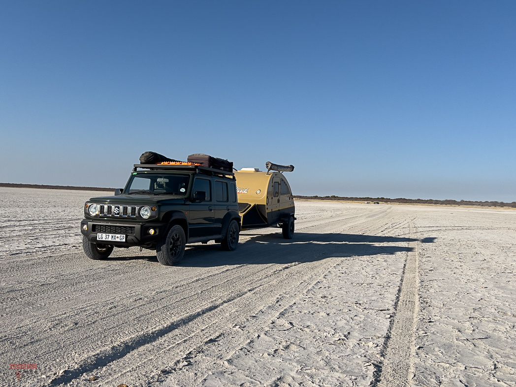 Suzuki Jimny 5-door towing a teardrop camping trailer across a salt pan in Southern Africa