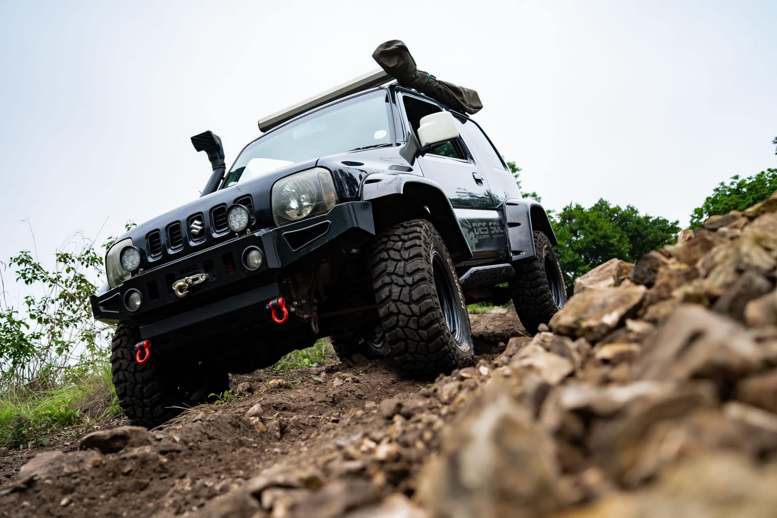 A lifted older Suzuki Jimny with a snorkel and mud tyres climbing a rocky track