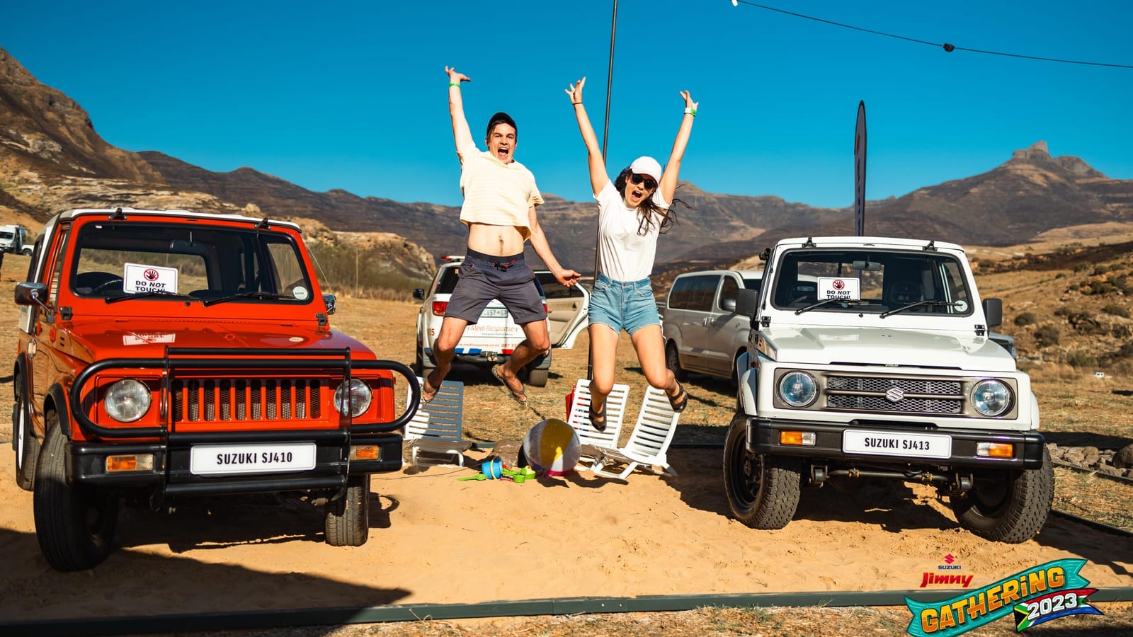A red Suzuki SJ410 and a white SJ413 on show at the 2023 Jimny Gathering in Clarens, with two people jumping for joy between them