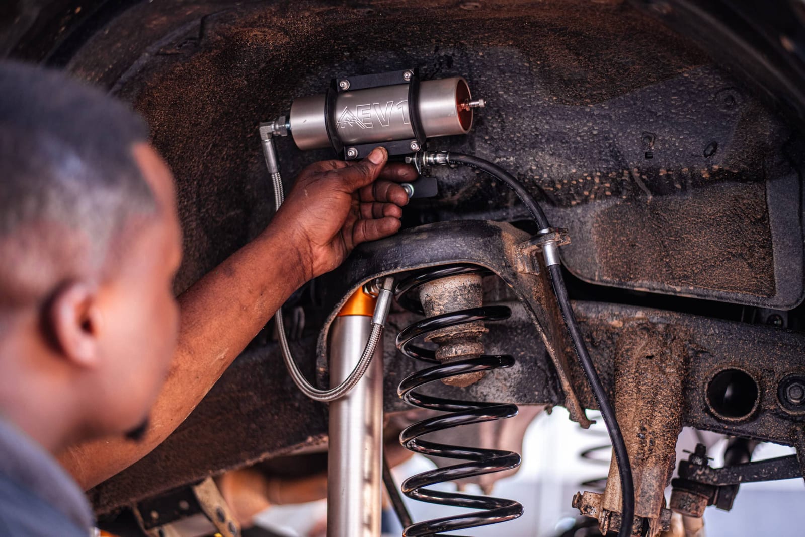 A fitter tightening a shock with a remote oil canister inside a Jimny wheel arch