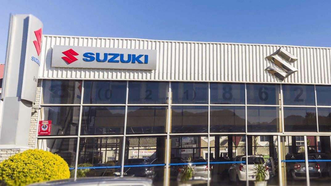 The front of a Suzuki dealership with a glass showroom and Suzuki signs under a blue sky