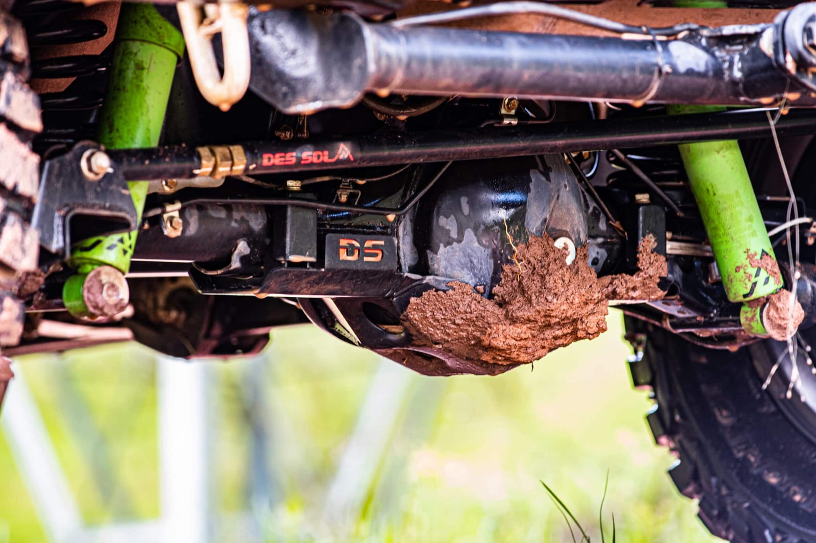 Underneath a lifted Suzuki Jimny: a steel diff guard caked in mud, with green shock absorbers either side