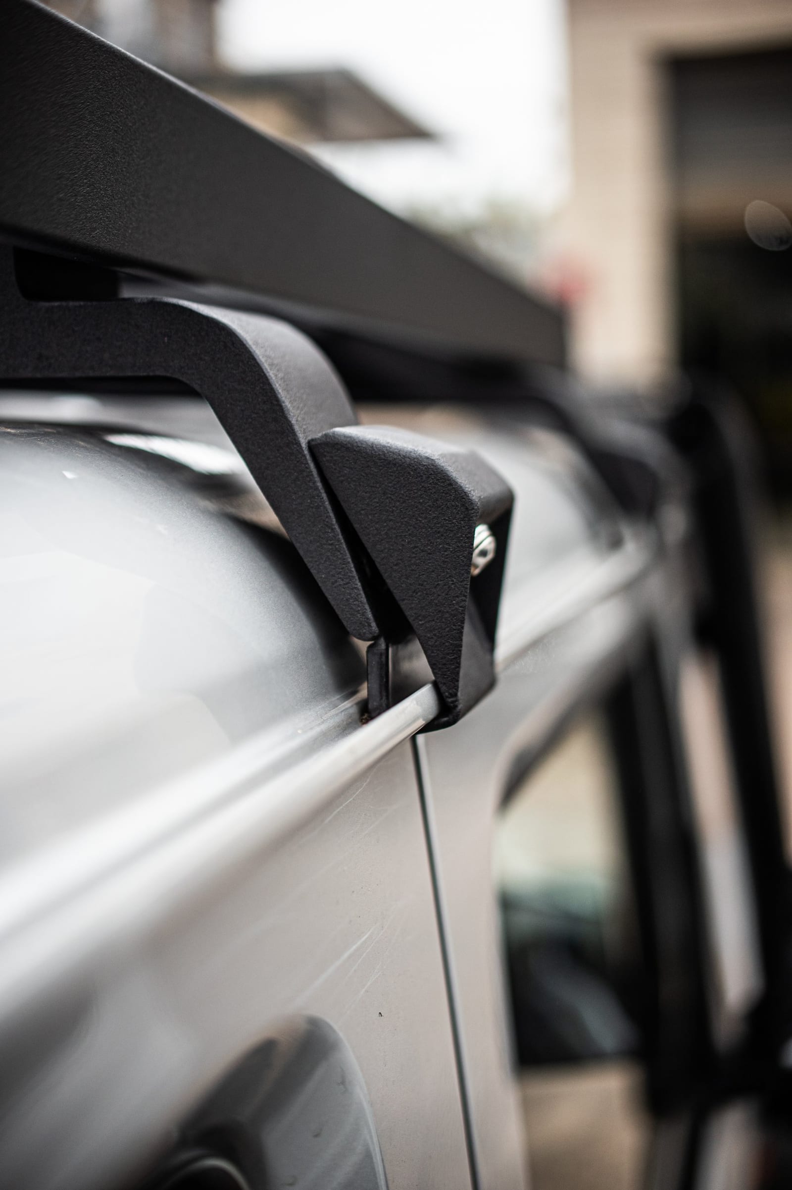 Close-up of a black roof rack bracket clamped over the rain gutter of a silver current Suzuki Jimny