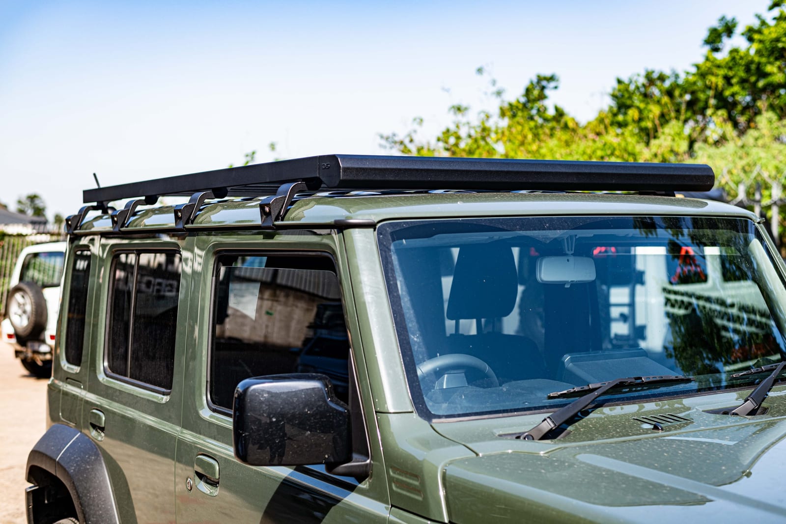 Side view of a green Suzuki Jimny 5-door with a long flat roof rack and a row of mounting brackets along the rain gutter