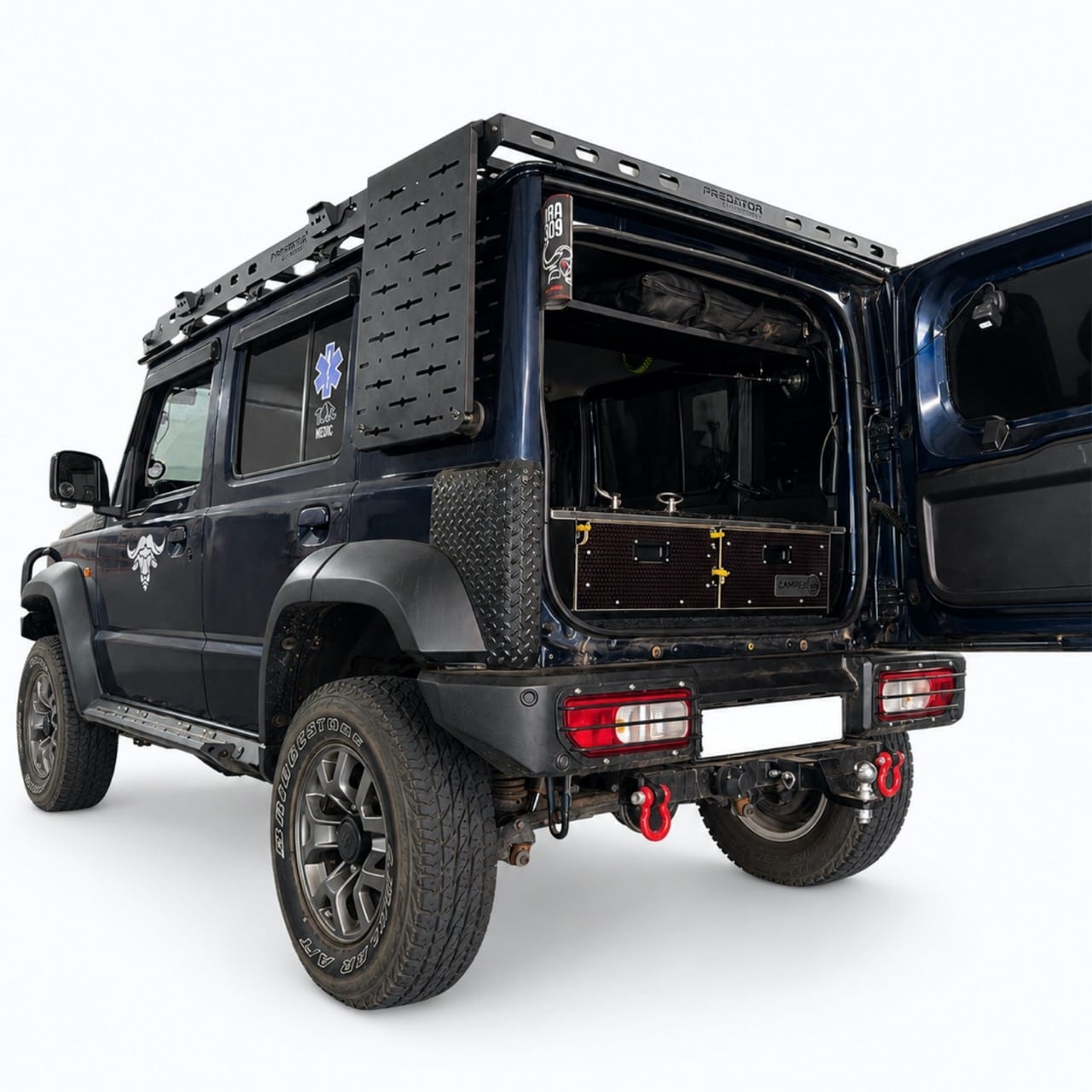 A lifted navy Suzuki Jimny 5-door seen from the rear three-quarter with the back door open, showing a drawer system in the boot and a Molle panel on the side window