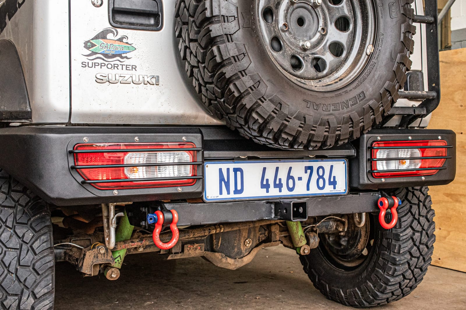 The rear of a silver Suzuki Jimny with a black steel bumper, a square tow hitch under the number plate and red recovery shackles on each side