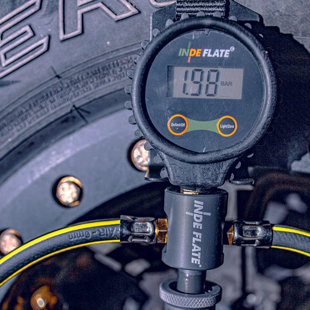 A digital tyre deflator gauge screwed onto a tyre valve, its screen showing a reading in bar