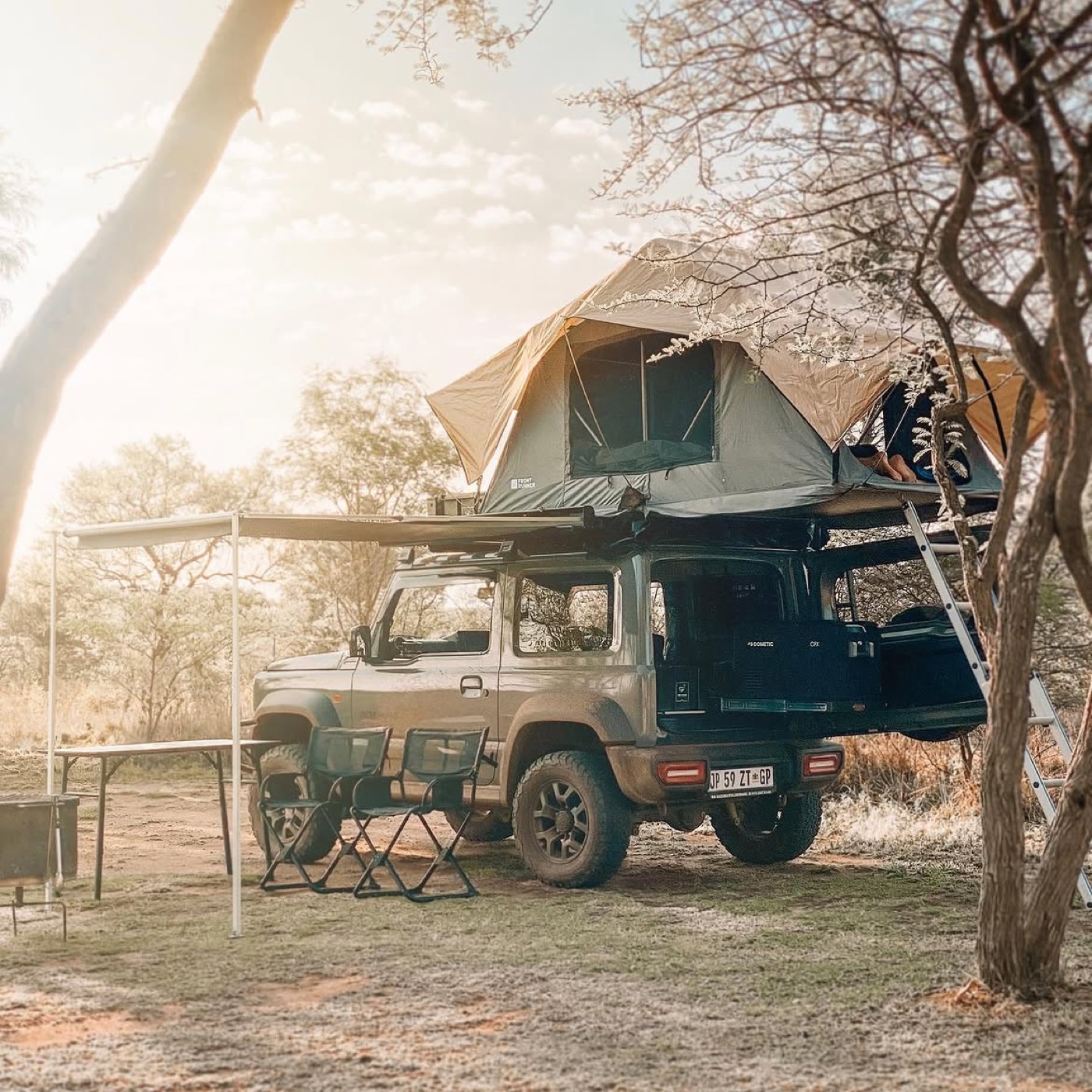 A Suzuki Jimny 3-door camped in the bushveld with a Front Runner rooftop tent deployed and awning out — photo by Roaming Horizons