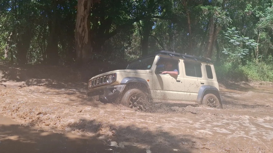 A Suzuki Jimny tackling a muddy water crossing off-road